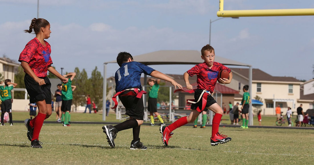Kids in red and blue jerseys playing youth flag football on a grass field