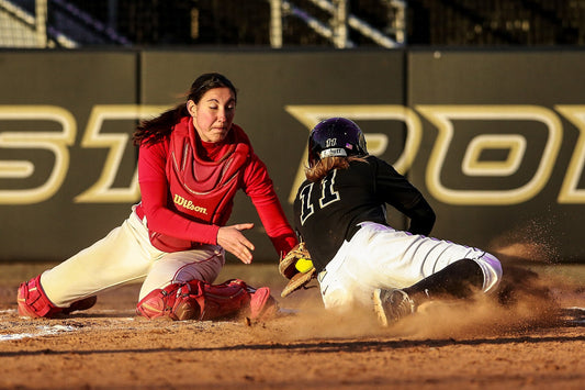 College softball catcher reaches to tag a runner sliding into home plate